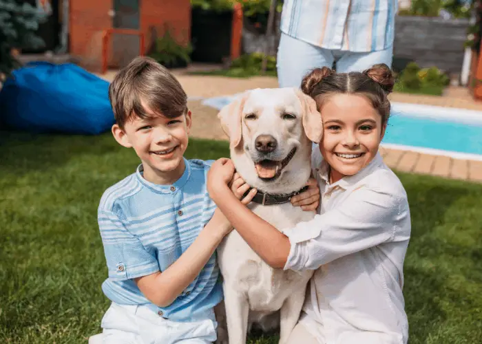 2 kids hugging a labrador retreiver