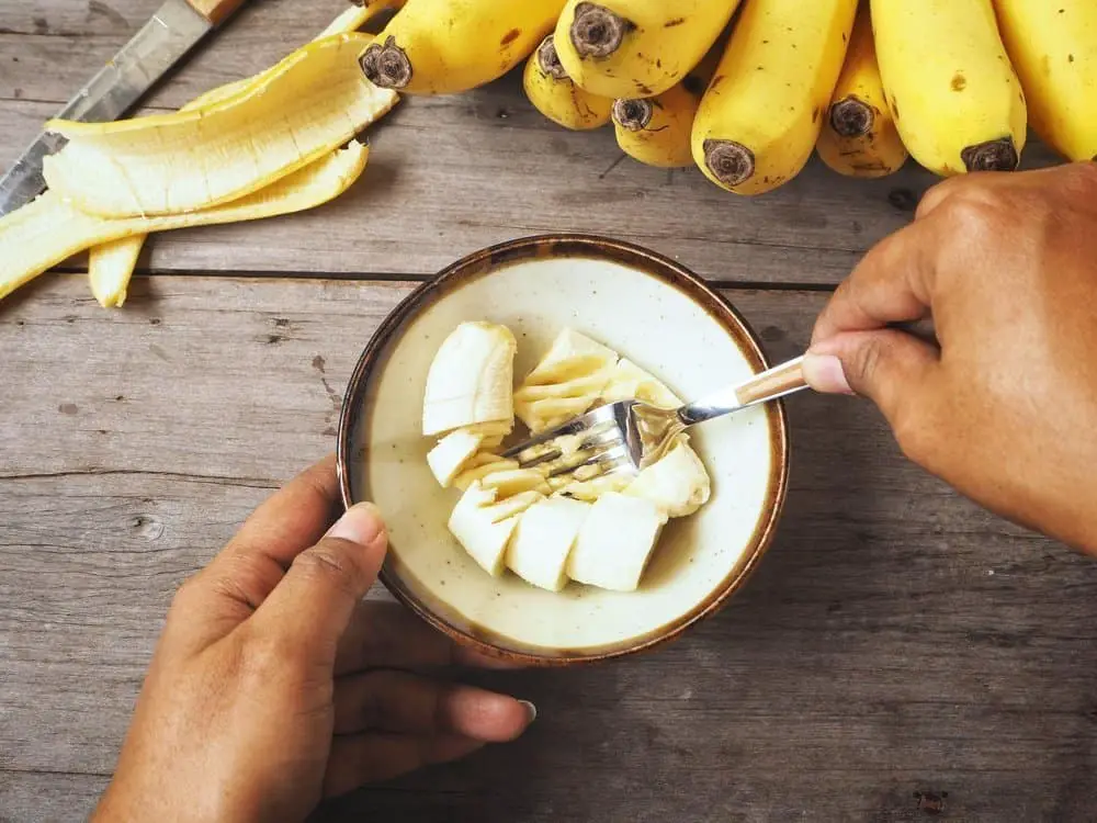 Woman mashing banana in bowl on wooden table