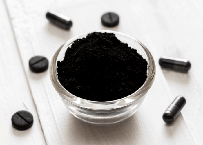 activated charcoal powder in a bowl with 3 tablets and 3 capsules of activated charcoal around it