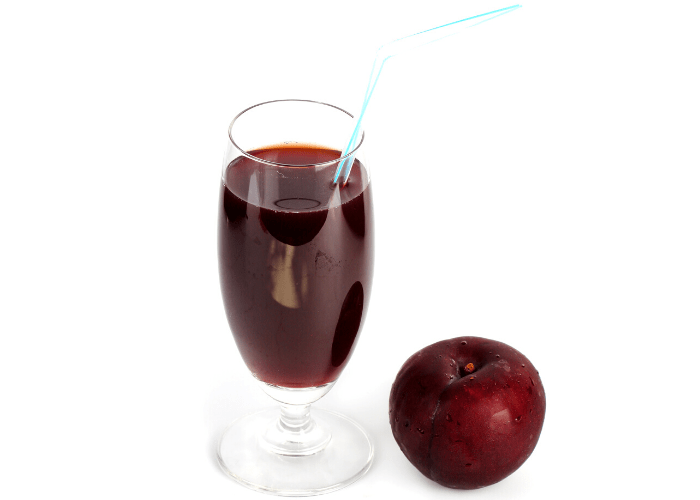 fresh prune juice in a cup with straw and a plum beside it on white background